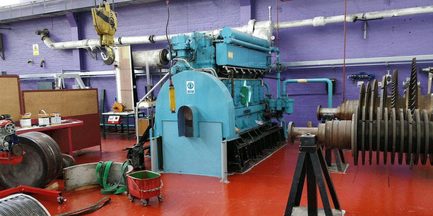 A large industrial engine sits in a workshop on red flooring.